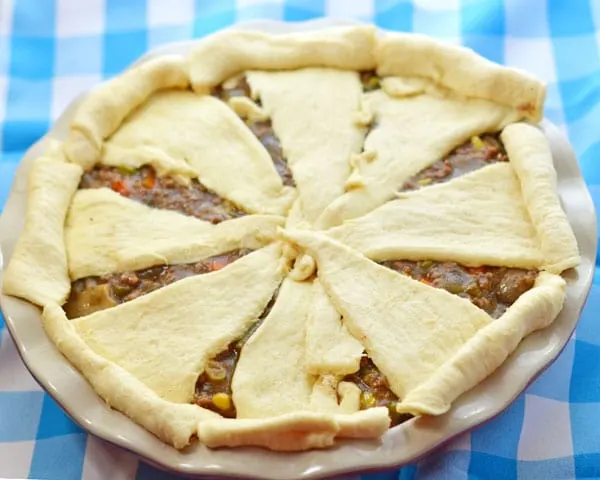 The whole unbaked beef pot pie in a ceramic red and white pie plate on a blue and white checkered background.