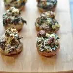 Baked spinach and sausage stuffed mushrooms on a bamboo cutting board.