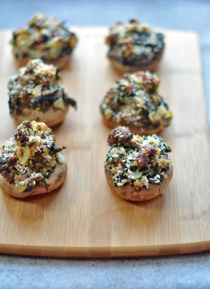 Baked spinach and sausage stuffed mushrooms on a bamboo cutting board.