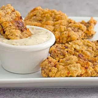 chicken fried steak fingers on a platter with a cup of cream gravy for dipping