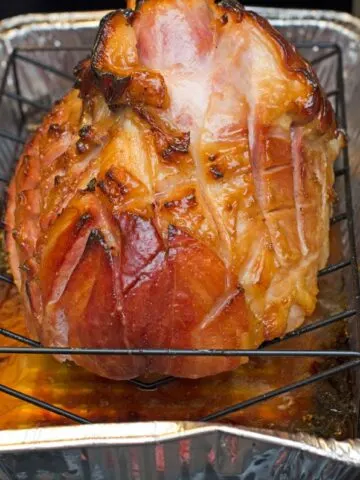 Ham that has been cooked with the brown sugar glaze on a rack in a foil baking pan.