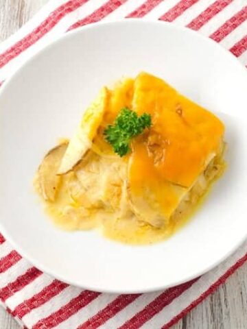 A serving of scalloped potatoes on a white round plate with a sprig of parsley on top.