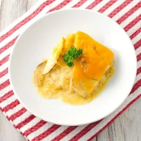 A serving of scalloped potatoes on a white round plate with a sprig of parsley on top.