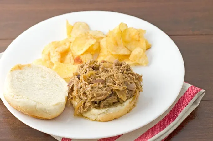 pulled pork sitting open face on a hamburger bun on a round white plate on a dark wood background