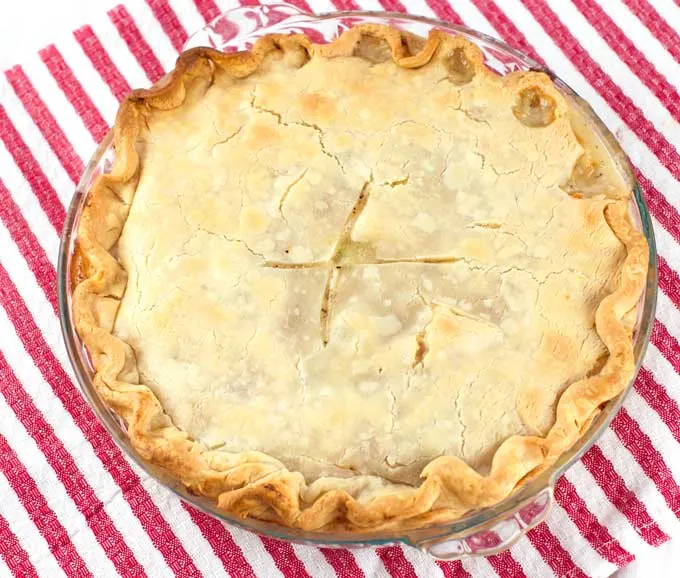 A whole baked chicken pot pie in a glass pie pan sitting on a red and white striped towel.
