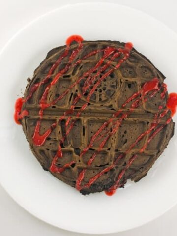 death star chocolate waffle topped with a drizzle of strawberry sauce on a white plate