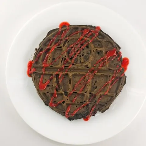 death star chocolate waffle topped with a drizzle of strawberry sauce on a white plate