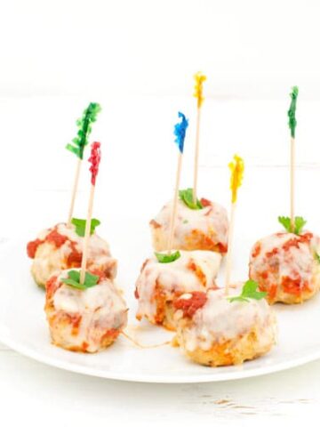 Prepared chicken parmesan meatballs on a white plate with toothpicks for easy appetizer eating