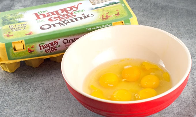 organic happy egg co eggs cracked into a red bowl with cream intereior