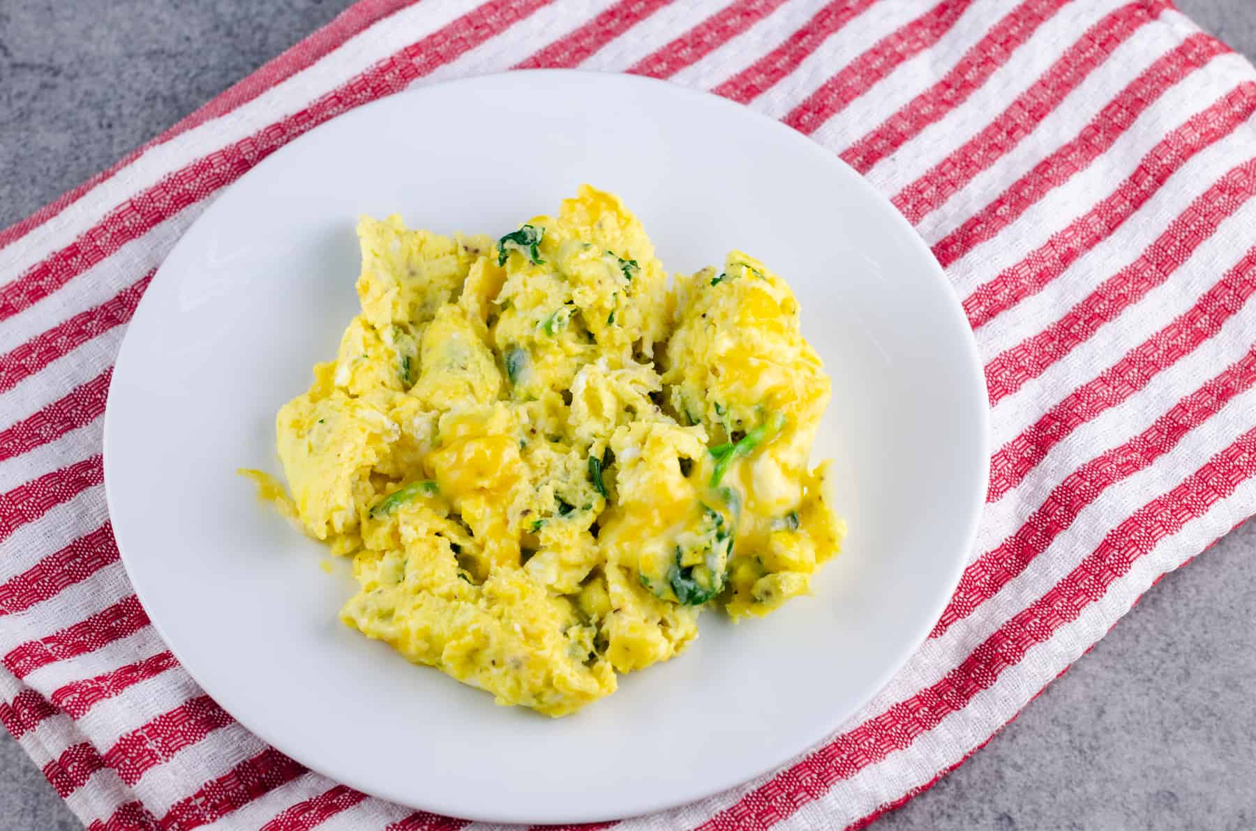 Cooked eggs on a white plate sitting on a red and white striped towel on a light gray background