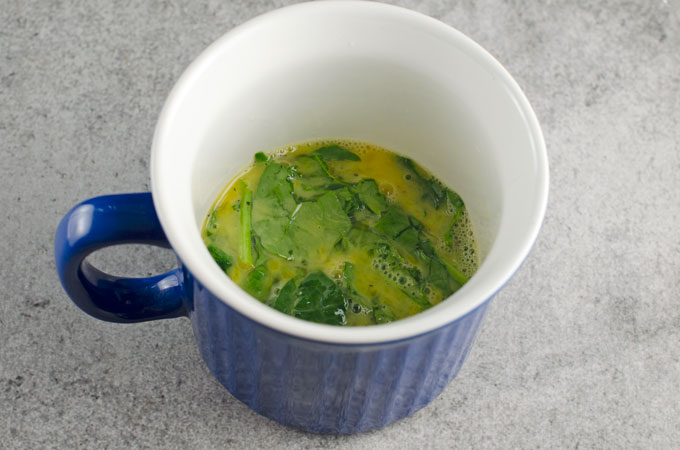 uncooked scrambled eggs with spinach getting ready to microwave