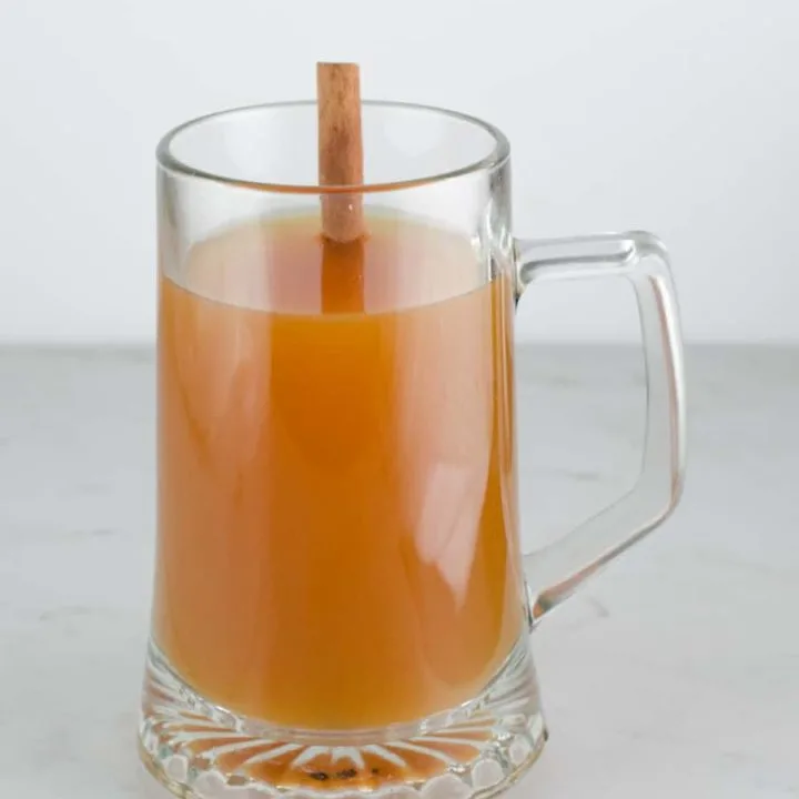 front view of a glass m ug of spiced apple cider tea with a cinnamon stick.