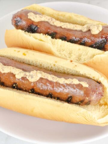 Two hot dog buns filled with honey mustard beer glazed bratwurst topped with dijon mustard.