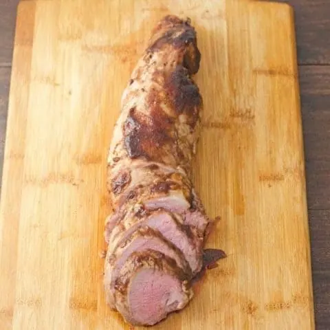 Partially sliced pork tenderloin with a balsamic apple butter glaze on a wood cutting board.