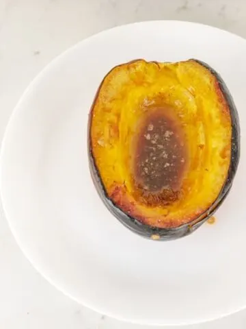Half of a baked brown sugar acorn squash on a round white plate.