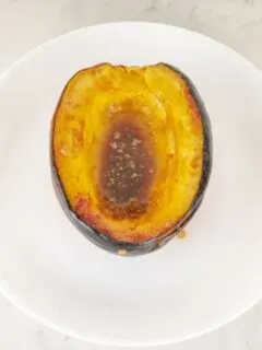 Half of a baked brown sugar acorn squash on a round white plate.