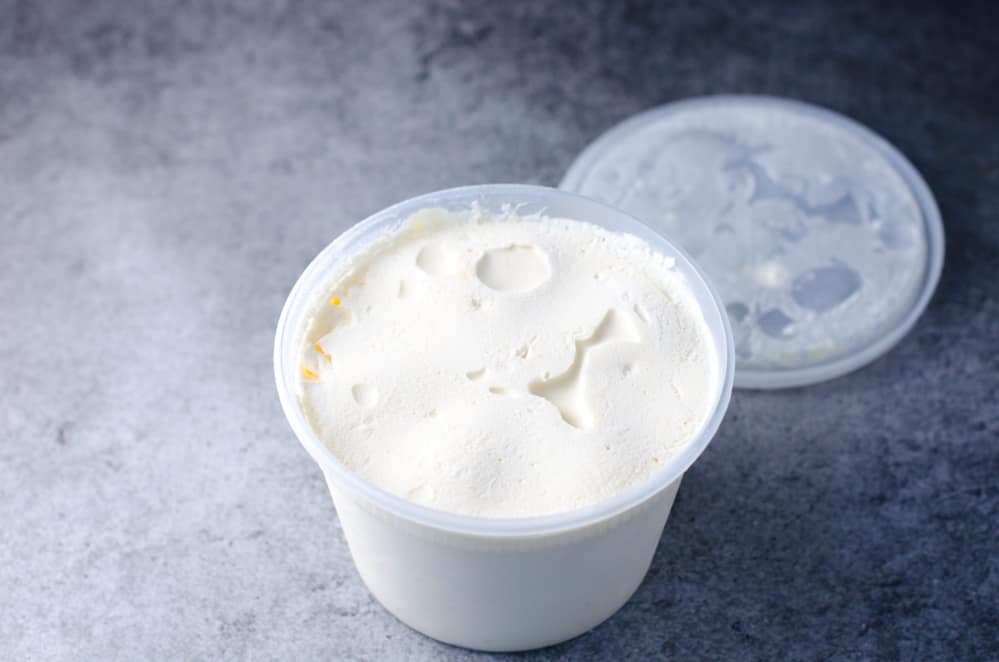 vanilla ice cream in a clear plastic container on a gray background