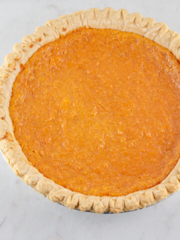 A whole sweet potato pie on a marble surface.
