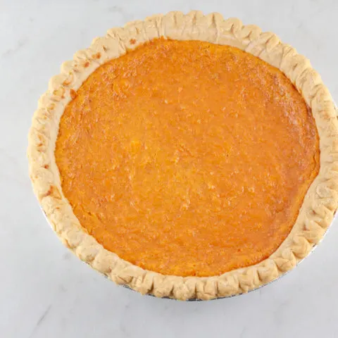 A whole sweet potato pie on a marble surface.