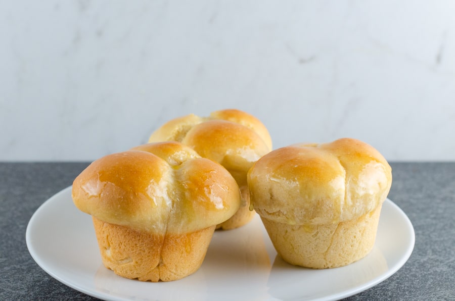 Homemade Cloverleaf Rolls Recipe with the rolls baked and brushed with butter on a white plate ready to serve