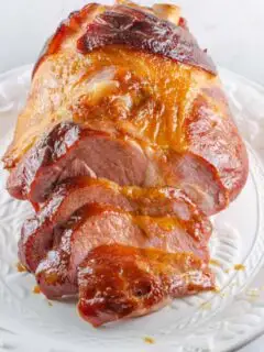 Brown sugar glazed ham partially sliced on a serving platter.