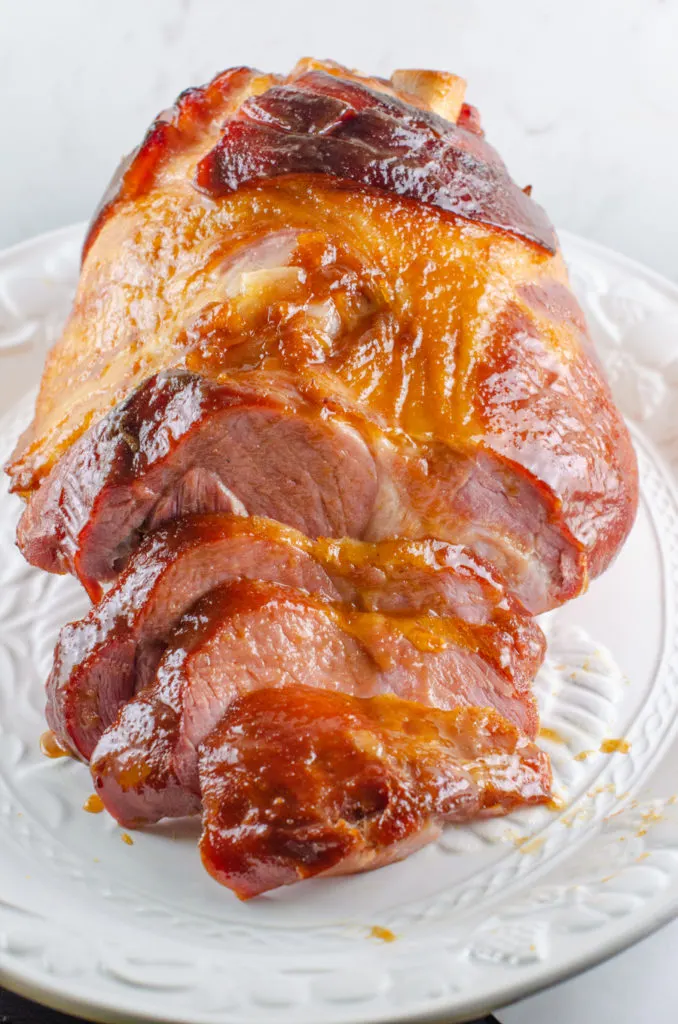 large ham partially sliced covered in the ham glaze and placed on a white platter