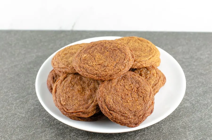 White plate on a black slate surface and marble background with the ginger cookies stacked on top.