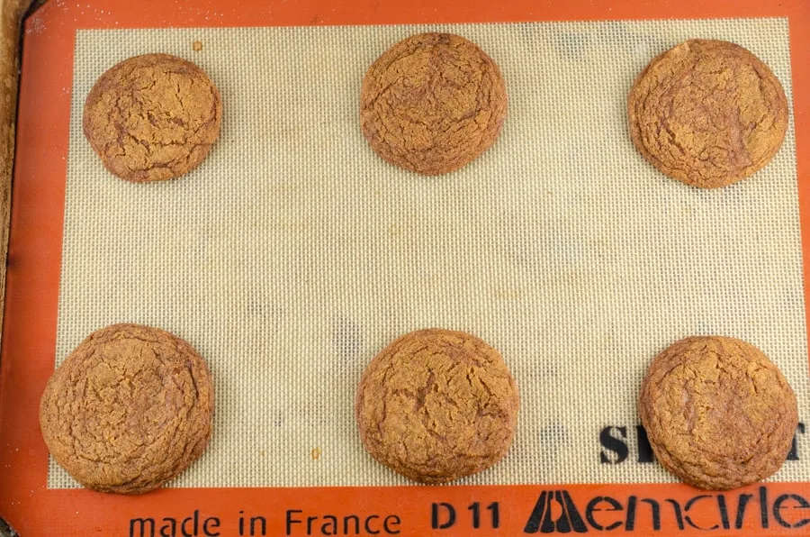 Baked ginger cookies on a silpat in a halfsheet baking pan cooling.