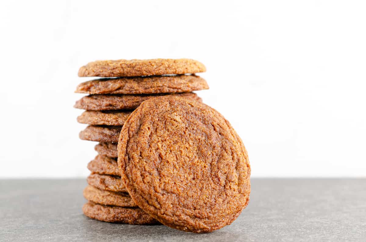stack of 10 crispy ginger molasses cookies stacked on each other with 1 standing to the side against them