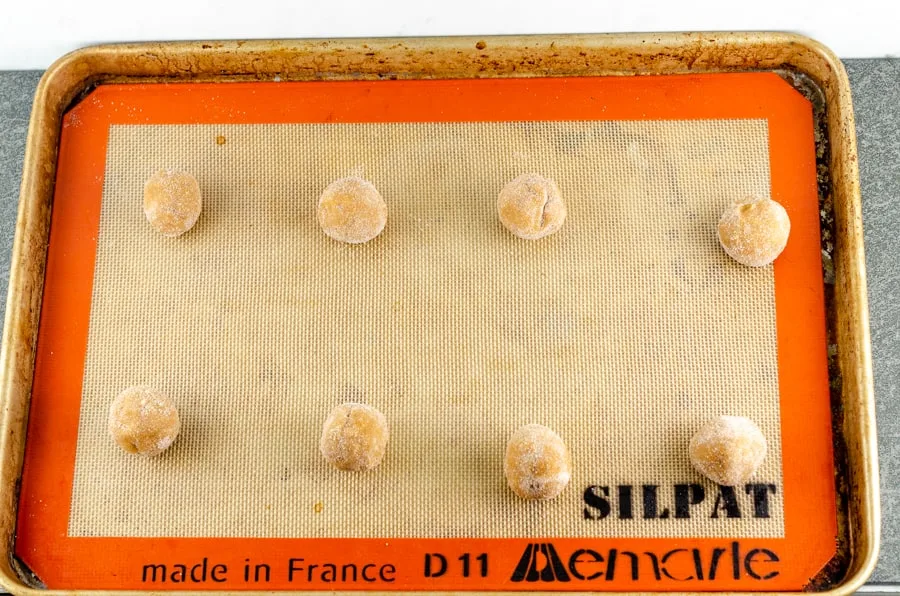 Rolled cookie dough balls on a silpat sheet in a half sheet baking pan ready to bake.