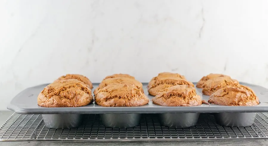 unglazed baked gingerbread muffins sitting in the muffin tin on a baking rack