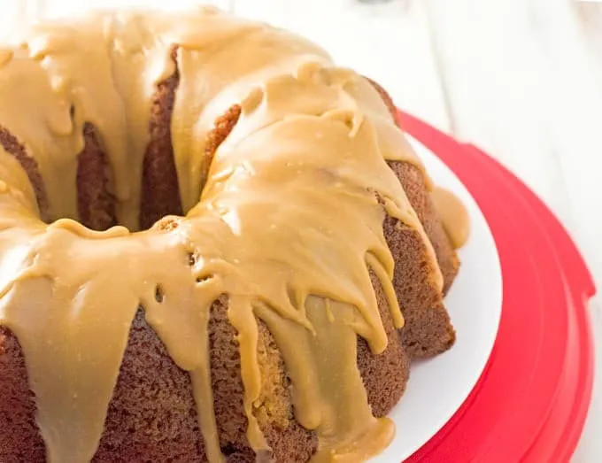 spice bundt cake with salted caramel glaze sitting on a white plate on top of a red plastic cake holder bottom