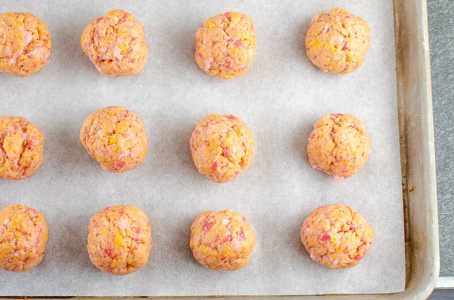 Uncooked sausage balls on a parchment lined baking sheet ready to be baked.