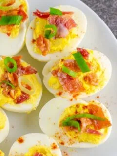 Closeup of completed bacon deviled eggs garnished with green onion and crisp bacon.