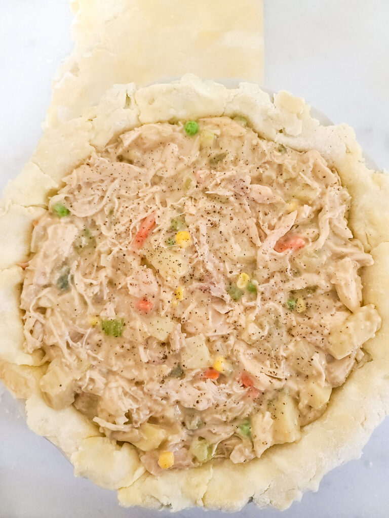 Unbaked chicken pie without the top crust sitting on a floured marble surface.