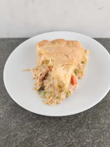 An overhead shot of a slice of baked chicken pot pie with the tip facing the front on a small white round plate on a slate surface and marble background.