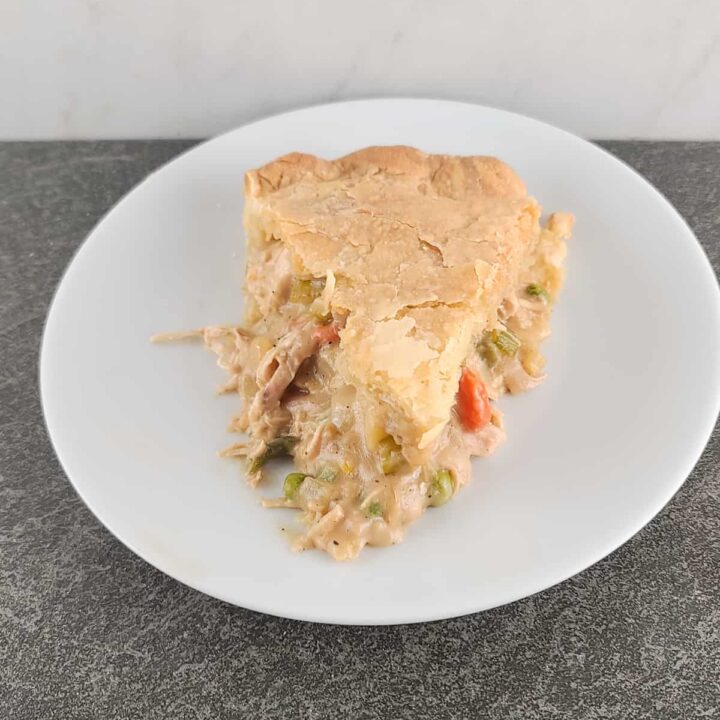 An overhead shot of a slice of baked chicken pot pie with the tip facing the front on a small white round plate on a slate surface and marble background.