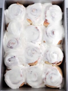 baked cinnamon rolls in a 9 by 13 slathered with cream cheese frosting