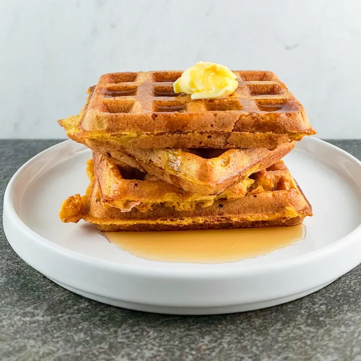 A stack of pumpkin waffles with butter and maple syrup.