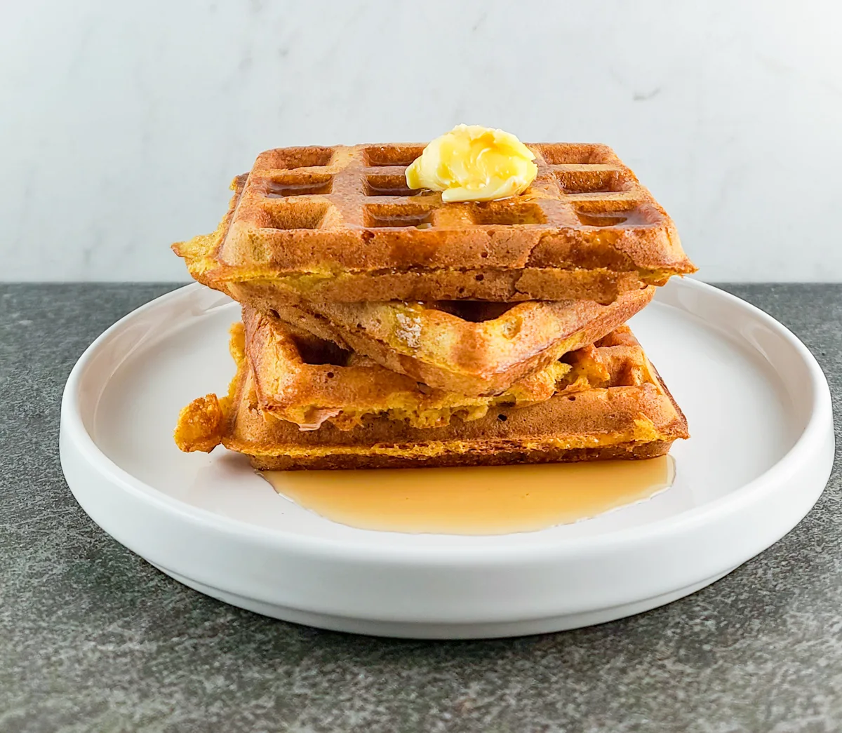 A stack of pumpkin waffles with butter and maple syrup.