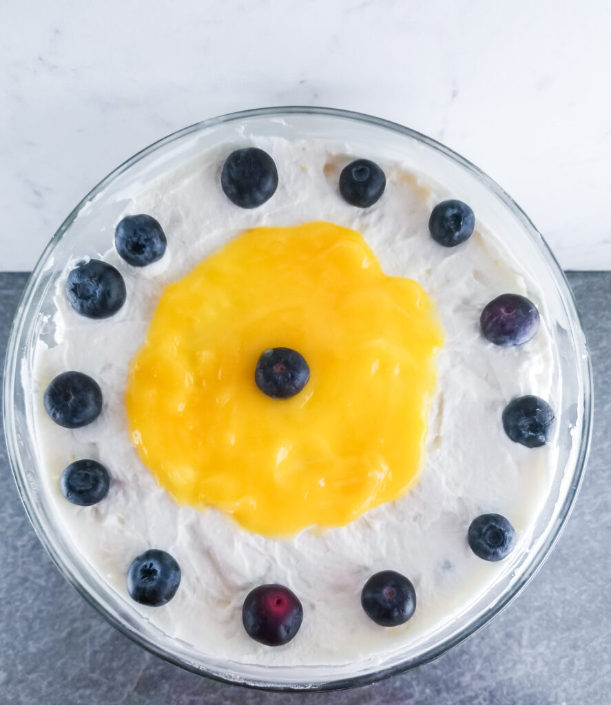 overhead shot of finished lemon blueberry trifle in a clear glass trifle bowl on a slate surface with marble background