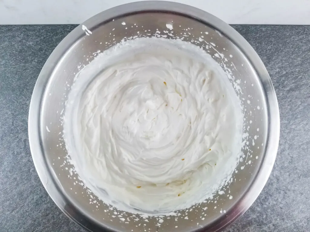prepared whipped cream in a stainless steel bowl on a slate surface with marble background
