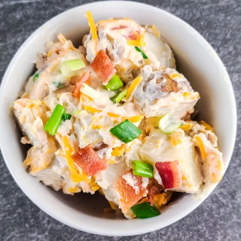 prepared baked potato salad in a small round white bowl on a black slate surface