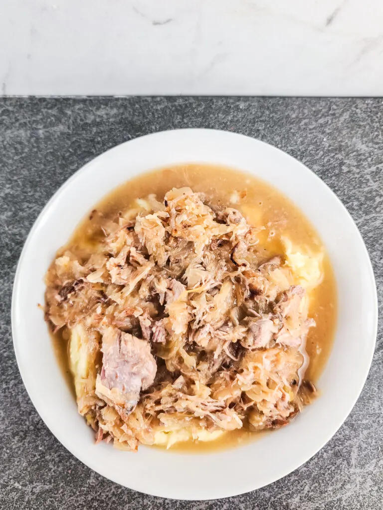 cooked pork and sauerkraut served over mashed potatoes in a shallow white bowl on a black slate background