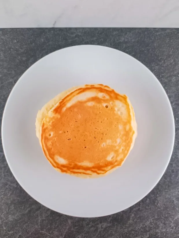 Overhead shot of a stack of pancakes on a white round plate.