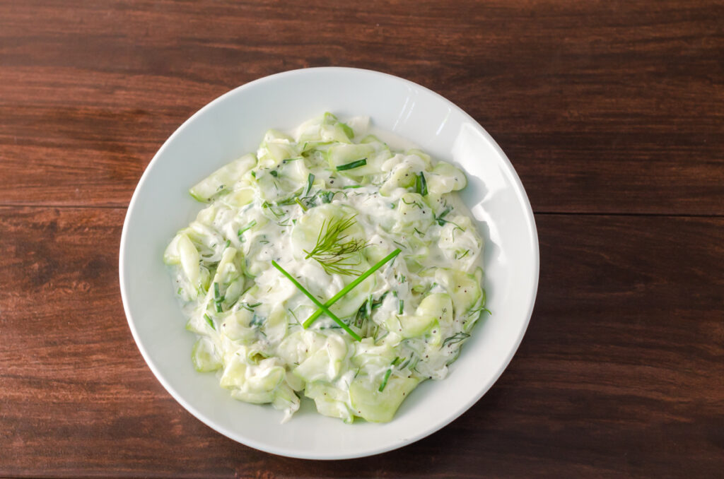 Creamy cucumber salad in a white round bowl garnished with fresh chives and dill.