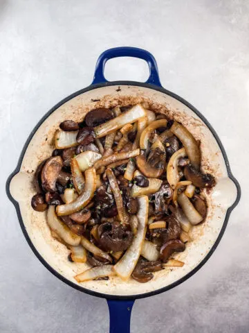 sauteed mushrooms and onions in a blue and white cast iron skillet topped with fresh thyme