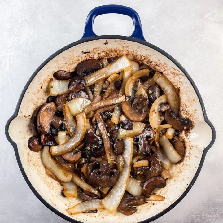 sauteed mushrooms and onions in a blue and white cast iron skillet topped with fresh thyme