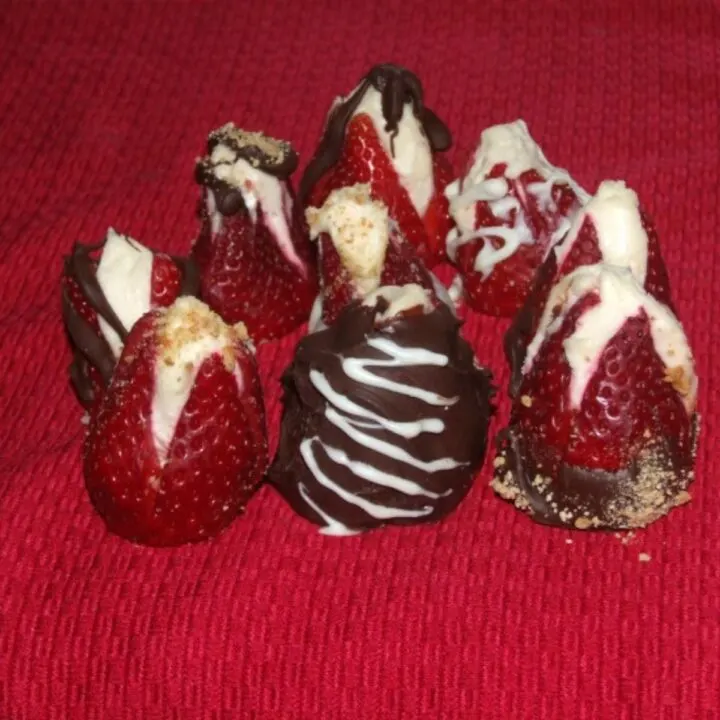 Several cheesecake stuffed strawberries with some dipped or drizzled in chocolate on a red background