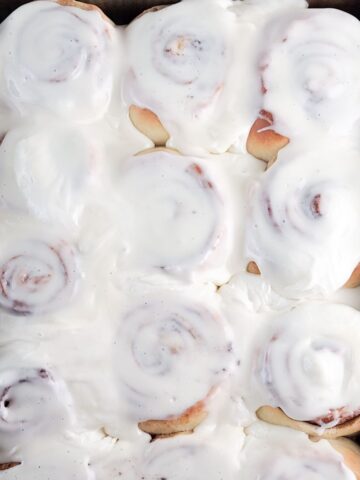 A rectangular pan of baked cinnamon rolls slathered with a lot of cream cheese frosting.
